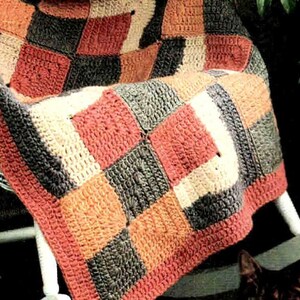 May include: A handmade crochet blanket featuring a repeating pattern of square motifs in shades of charcoal gray, cream, and muted coral. The textile is constructed from individual yarn squares joined together to form a textured, geometric grid design.