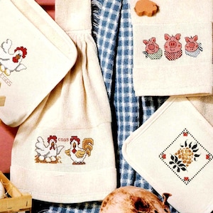 May include: A collection of off-white kitchen textiles with cross-stitched designs. The items include pot holders, a towel, and a hanging towel, each featuring images of chickens, pigs, and a pineapple. The pot holder has the text "FRESH EGGS".