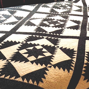 May include: A close-up of a handmade quilt with a geometric pattern. The quilt features a repeating design of black and white shapes, including triangles and stars, creating a striking contrast. The quilt's texture is visible, suggesting a soft, comfortable feel.