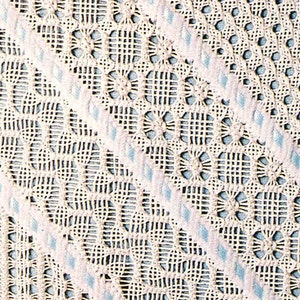 May include: Close-up of a white crocheted fabric with a repeating pattern of circles and squares. The fabric has a delicate, lacy texture.