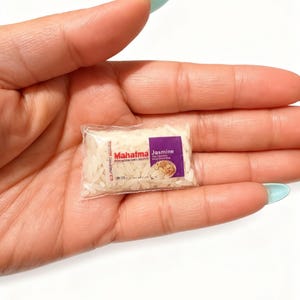 May include: A miniature, clear plastic bag filled with white jasmine rice grains. The bag features a small label with the red text Mahatma and purple text Jasmine, along with a small graphic of cooked rice, mimicking a standard food package.