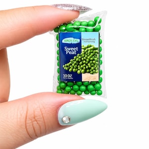 K&ouml;nnte beinhalten: Ein Miniaturbeutel mit "Sweet Peat" Erbsen, der zwischen Fingern gehalten wird. Der Beutel ist transparent mit einem blau-wei&szlig;en Etikett mit der Aufschrift "BINDS EYG Steamfresh nanaming" und "10 OZ". Gr&uuml;ne Erbsen sind im und um den Beutel sichtbar.