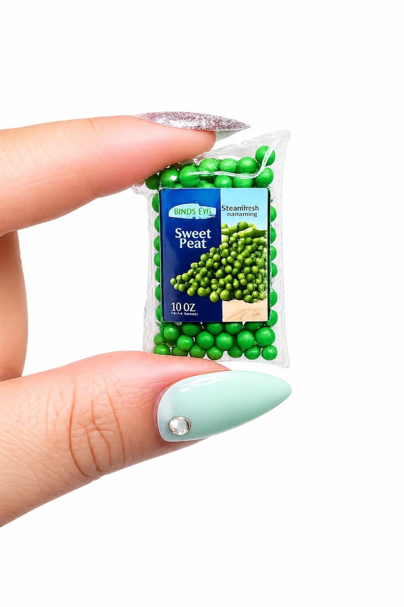 K&ouml;nnte beinhalten: Ein Miniaturbeutel mit "Sweet Peat" Erbsen, der zwischen Fingern gehalten wird. Der Beutel ist transparent mit einem blau-wei&szlig;en Etikett mit der Aufschrift "BINDS EYG Steamfresh nanaming" und "10 OZ". Gr&uuml;ne Erbsen sind im und um den Beutel sichtbar.