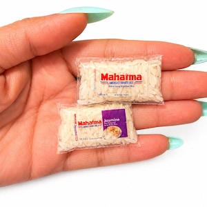 May include: Two miniature clear plastic packets filled with white rice grains. The top packet features the red and blue Mahatma logo with the text America's Favorite Rice. The bottom packet has a purple label with the text Mahatma Jasmine.