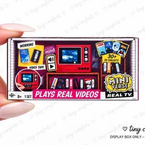 May include: A rectangular Mini Verse Real TV toy packaging box featuring a red miniature television set, a shelf with various small video tapes, and text including "WORKING", "30+ TO COLLECT!", and "PLAYS REAL VIDEOS" printed on the front.