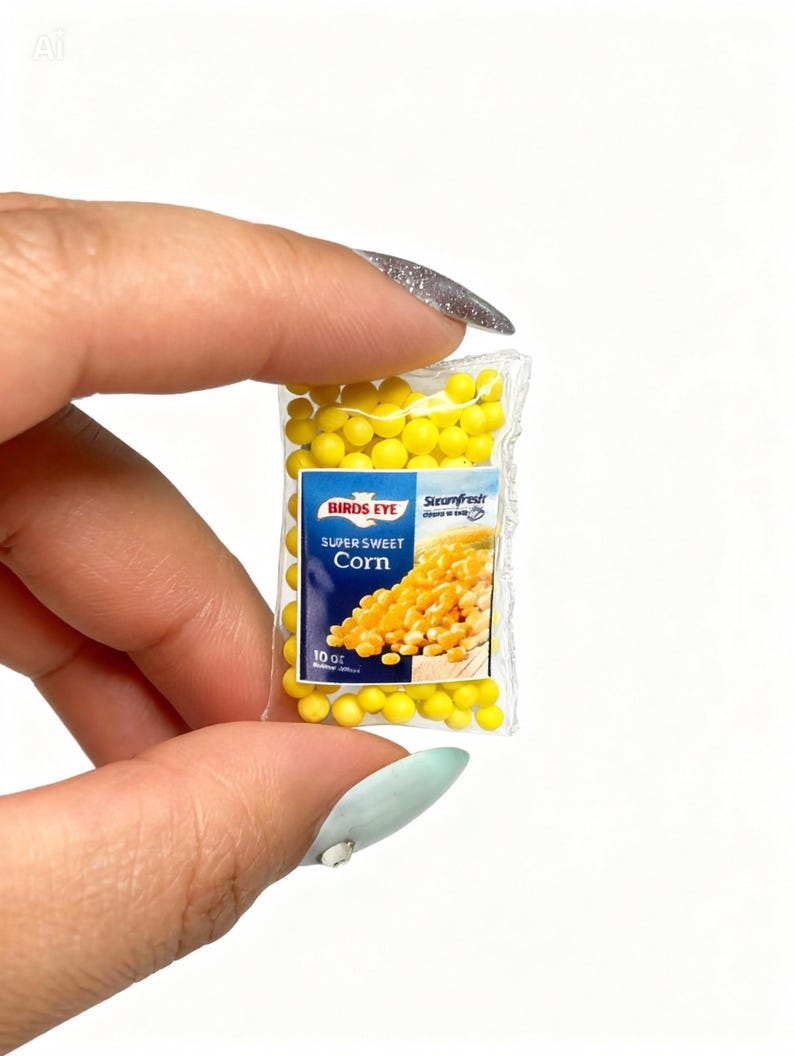 K&ouml;nnte beinhalten: Miniaturbeutel mit Birds Eye Super Sweet Corn. Der transparente Plastikbeutel enth&auml;lt gelbe Maisk&ouml;rner und hat ein blau-wei&szlig;es Etikett. Auf dem Etikett steht "Birds Eye" und "Super Sweet Corn". Der Beutel wird zwischen Fingern gehalten.