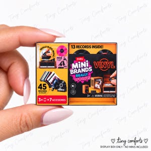 May include: A rectangular Zuru Mini Brands Really Works Vinyl toy box featuring a yellow and black color scheme. The packaging displays text including 13 RECORDS INSIDE, 45 RECORDS TO COLLECT, and 3+7 ACCESSORIES, with illustrations of miniature record players.