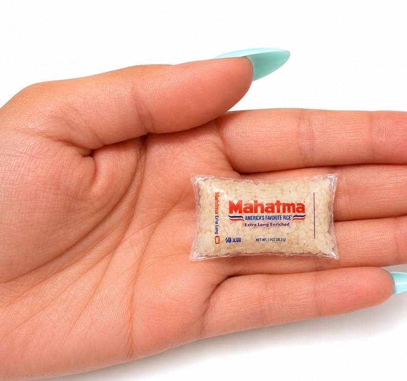 May include: A miniature clear plastic bag filled with white rice grains, featuring the red and blue Mahatma logo, the text America's Favorite Rice, Extra Long Enriched, and a net weight of 1 oz (28.3 g) printed on the front of the small package.