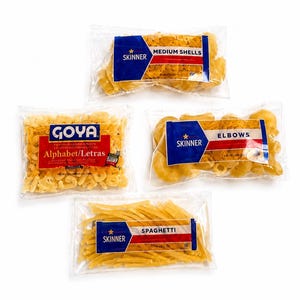May include: Four clear plastic bags of dry pasta arranged on a white surface. The bags include Skinner brand medium shells, elbows, and spaghetti, alongside a Goya brand bag of alphabet pasta. Each package features blue and red branding labels.