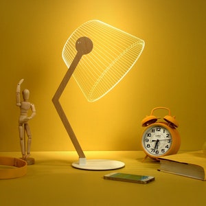 May include: A modern desk lamp with a wooden frame and a white, illuminated lampshade. The image also features a yellow alarm clock, headphones, a smartphone, a wooden mannequin, a book, and a smiley face ball, all on a yellow surface.