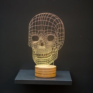 May include: A wireframe skull shaped night light with a wooden base. The light is on and glowing yellow.
