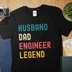 May include: Black t-shirt with a vintage-style graphic that reads "Husband Dad Engineer Legend".
