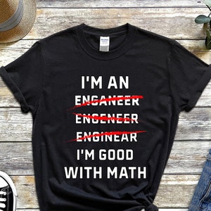 Pode incluir: Camiseta preta com texto branco que diz "Eu sou um Enganeer Engineer Enginear Eu sou bom em matemática". As palavras "Enganeer", "Engineer" e "Enginear" estão riscadas com linhas vermelhas.