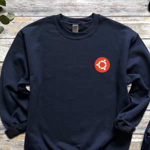 May include: A navy blue sweatshirt with a red circle logo featuring a white stylised symbol of a circle with six smaller circles around it.