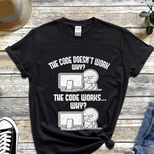 Könnte beinhalten: Schwarzes T-Shirt mit einer weißen Grafik einer Comicfigur an einem Computer. Der Text auf dem Shirt lautet "The code doesn't work. Why? The code works... Why?"