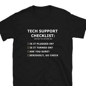 Op de afbeelding: Zwart T-shirt met witte tekst die "Tech Support Checklist: (Before you bother me)" luidt en een lijst met vragen: "Is it plugged in?", "Is it turned on?", "Are you sure?", "Seriously, go check."