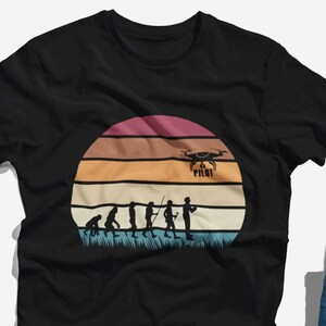 Może przedstawiać: Czarny T-shirt z grafiką w stylu vintage przedstawiającą zachód słońca i ewolucję człowieka, która kończy się na osobie trzymającej drona z napisem "Drone Pilot".