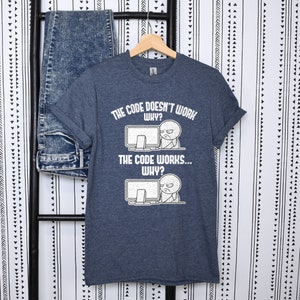 Peut inclure: Un t-shirt bleu fonc&eacute; avec un graphique blanc d'un personnage de dessin anim&eacute; regardant un &eacute;cran d'ordinateur avec confusion. Le texte sur le t-shirt est "The code doesn't work... Why?" et "The code works... Why?"
