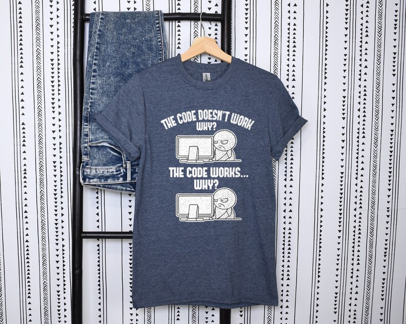 Peut inclure: Un t-shirt bleu fonc&eacute; avec un graphique blanc d'un personnage de dessin anim&eacute; regardant un &eacute;cran d'ordinateur avec confusion. Le texte sur le t-shirt est "The code doesn't work... Why?" et "The code works... Why?"