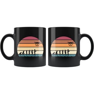 May include: Two black coffee mugs featuring a retro sunset design with a silhouette of a person holding a drone. The text "Drone Pilot" is printed on the mug.