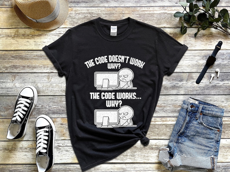 Peut inclure: T-shirt noir avec un graphique blanc d'une personne de dessin anim&eacute; devant un ordinateur. Le texte sur le t-shirt est "The code doesn't work. Why? The code works... Why?"