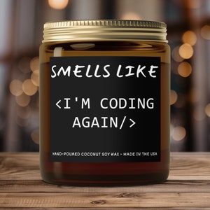 Peut inclure: Un bocal en verre brun contenant une bougie avec une étiquette noire sur laquelle est inscrit "SMELLS LIKE <I'M CODING AGAIN/>" et "HAND-POURED COCONUT SOY WAX - MADE IN THE USA".