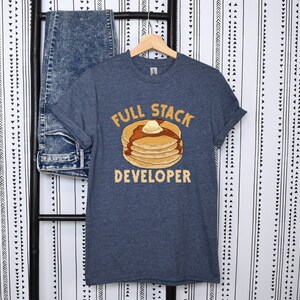 K&ouml;nnte beinhalten: Ein dunkelblaues T-Shirt mit einer Grafik eines Stapels Pfannkuchen mit Butter und Sirup. Der Text "Full Stack Developer" ist unter den Pfannkuchen gedruckt.