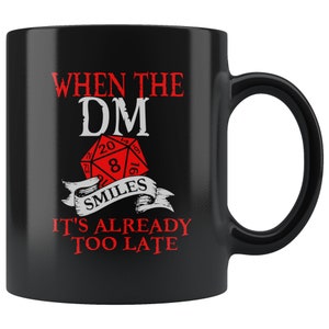 May include: Black ceramic coffee mug with a white design that says "When the DM smiles it's already too late". The design also includes a red 20-sided die.