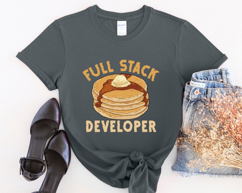 K&ouml;nnte beinhalten: Ein dunkelgraues T-Shirt mit dem Text "Full Stack Developer" und einer Grafik eines Stapels Pfannkuchen mit Butter und Sirup.