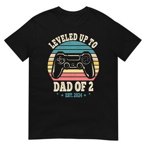 Pode incluir: Camiseta preta com um gráfico retrô de um controlador de videogame e o texto "Leveled Up To Dad Of 2 Est. 2024".