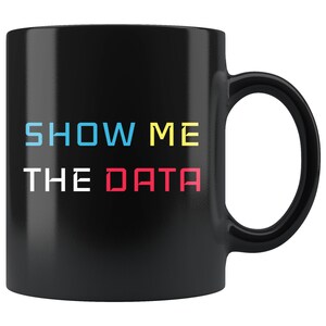 Könnte beinhalten: Schwarze Kaffeetasse mit dem Text "SHOW ME THE DATA" in bunten Buchstaben. Die Buchstaben sind in verschiedenen Farben: blau, gelb und rot.