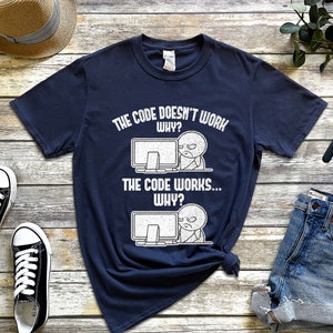Peut inclure: Un t-shirt bleu marine avec un graphique blanc d'un &eacute;cran d'ordinateur et un bonhomme b&acirc;ton. Le texte sur le t-shirt est "The code doesn't work. Why? The code works... Why?"