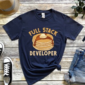 K&ouml;nnte beinhalten: Ein marineblaues T-Shirt mit einer Grafik eines Stapels Pfannkuchen und dem Text "Full Stack Developer".