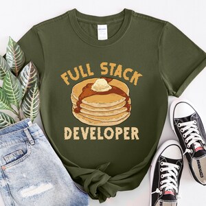 K&ouml;nnte beinhalten: Ein gr&uuml;nes T-Shirt mit dem Text "Full Stack Developer" und einem Cartoon-Bild eines Stapels Pfannkuchen mit Butter und Sirup.