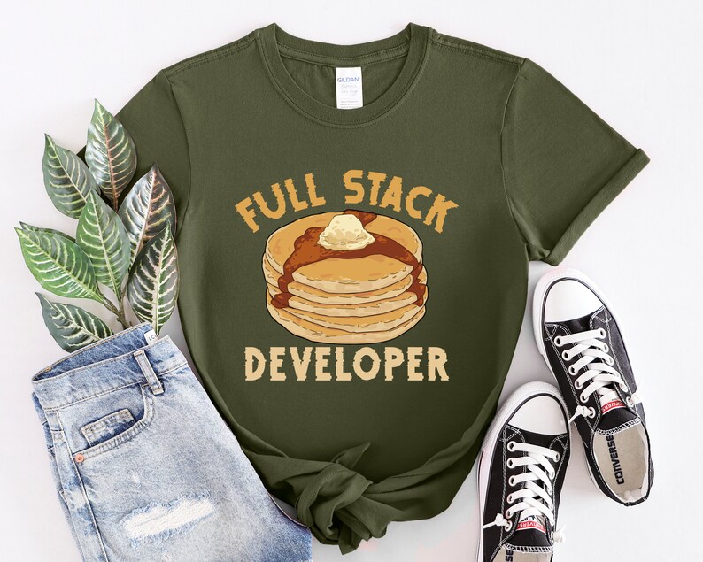 K&ouml;nnte beinhalten: Ein gr&uuml;nes T-Shirt mit dem Text "Full Stack Developer" und einem Cartoon-Bild eines Stapels Pfannkuchen mit Butter und Sirup.