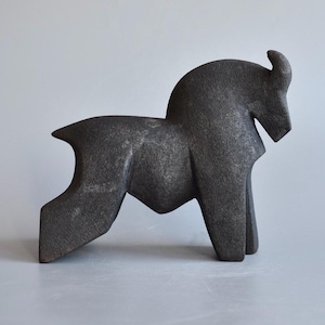 Könnte beinhalten: Eine dunkelgraue, stilisierte Skulptur eines Pferdes in stehender Pose. Die Skulptur hat ein geometrisches Design mit einem gebogenen Hals und einem einzelnen Horn. Das Pferd ist in vereinfachter Form dargestellt, mit eckigen Beinen und einem stromlinienförmigen Körper.