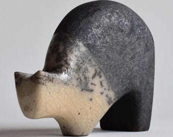 May include: A small, abstract ceramic sculpture with a black and white glaze. The sculpture has a rounded, organic shape and is reminiscent of a head or a figure.