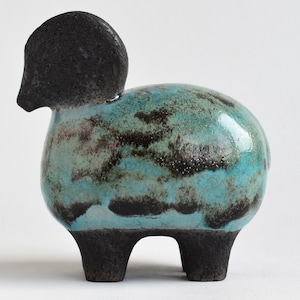 May include: A ceramic sheep ornament with a black head and legs. The body is a mottled turquoise with dark brown markings. The sheep has a rounded body and stands on three short legs. A decorative item.