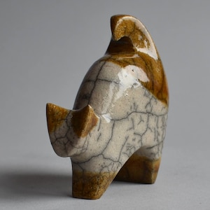 Pode incluir: Escultura em cerâmica de uma forma animal abstrata. A escultura apresenta um corpo creme com detalhes castanhos e um efeito craquelado. A peça tem uma parte traseira curva e uma cabeça pontiaguda, com uma pequena protuberância em forma de chifre.