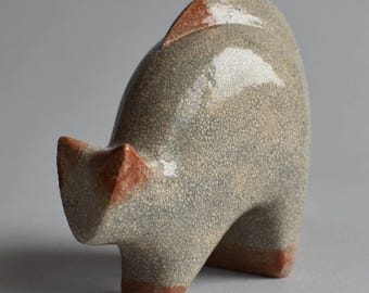 May include: A ceramic sculpture of an animal, possibly a cat or a pig, in a stylized form. The sculpture is primarily gray with a crackle glaze, and features accents of reddish-brown on the ears, tail, and feet. The piece has a smooth, rounded form.