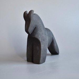 May include: A dark gray, abstract horse sculpture. The sculpture has a geometric design with a curved neck and a forward-leaning posture. The horse's body is solid and blocky, with a smooth, textured surface.