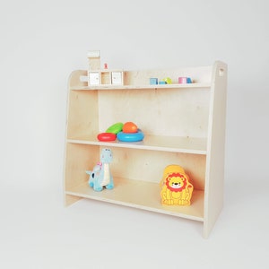 May include: A wooden three-shelf unit with rounded edges, featuring a blue dinosaur toy, a yellow lion toy, and colorful plastic toys on the shelves.