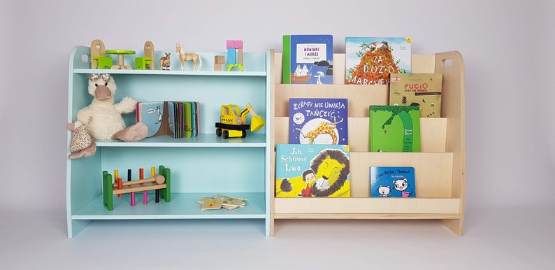 May include: Two wooden bookshelves, one light blue and one natural wood, with different sized shelves. The blue bookshelf has a stuffed duck, a wooden toy truck, and a wooden toy train on the shelves. The natural wood bookshelf has several children's books on the shelves, including "Za Duzo Marchewek" and "Pugio".