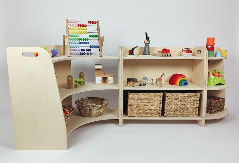 May include: A wooden toy shelf with curved shelves and a straight shelf unit. The shelves are filled with various toys, including a colorful abacus, a toy house, animal figurines, a rainbow arch, and baskets.