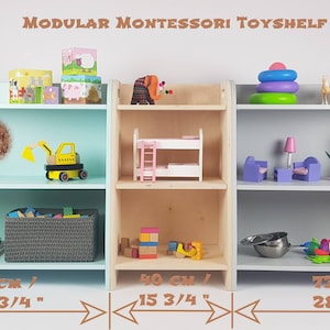 May include: Three modular Montessori toy shelves in different colors: light blue, natural wood, and gray. Each shelf has two shelves and measures 28 3/4 inches wide. The shelves are filled with various toys, including blocks, a toy truck, a dollhouse, a stacking ring toy, and stuffed animals.