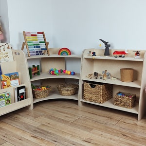 May include: A set of three wooden corner shelves with rounded edges. The shelves are filled with various toys, including a rainbow, a wooden abacus, and stuffed animals. The shelves are in a light wood finish and are perfect for a child's playroom.