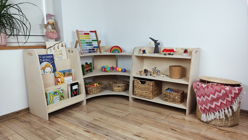 May include: A set of three wooden corner shelves with rounded edges. The shelves are filled with various toys, including a rainbow, a wooden abacus, and stuffed animals. The shelves are in a light wood finish and are perfect for a child's playroom.