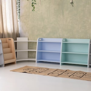 May include: Four corner shelves in different colors, including light blue, light green, white, and gray. The shelves are made of wood and have three shelves each. A brown rug with black numbers is in front of the shelves.