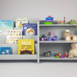 Pu&ograve; includere: Una libreria in legno grigia con due ripiani su ogni lato. Il lato sinistro ha un organizzatore di libri con diversi libri per bambini colorati. Il lato destro ha una variet&agrave; di giocattoli, tra cui una rana di peluche, un'anatra di peluche, una cucina giocattolo in legno e una pila di anelli colorati.