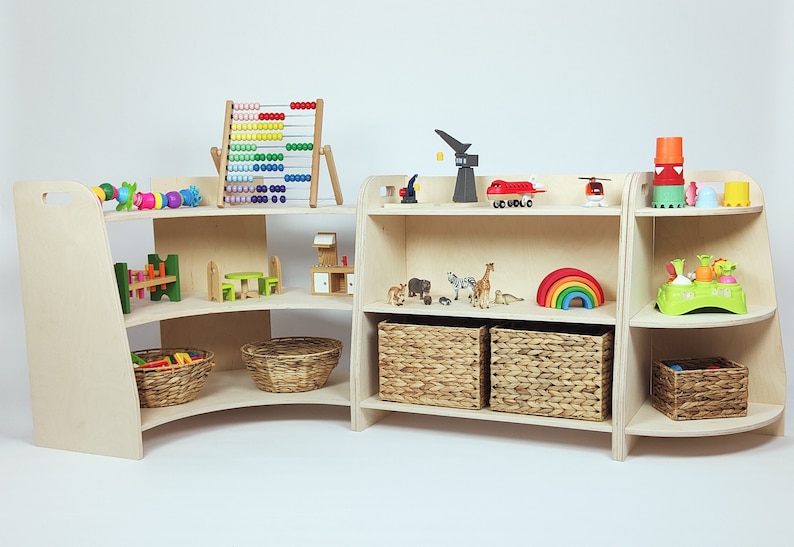 May include: A set of two wooden toy shelves with curved edges. The shelves are filled with various toys, including a rainbow, a wooden abacus, a toy crane, a toy airplane, and a toy car. The shelves are made of light wood and have a natural finish.